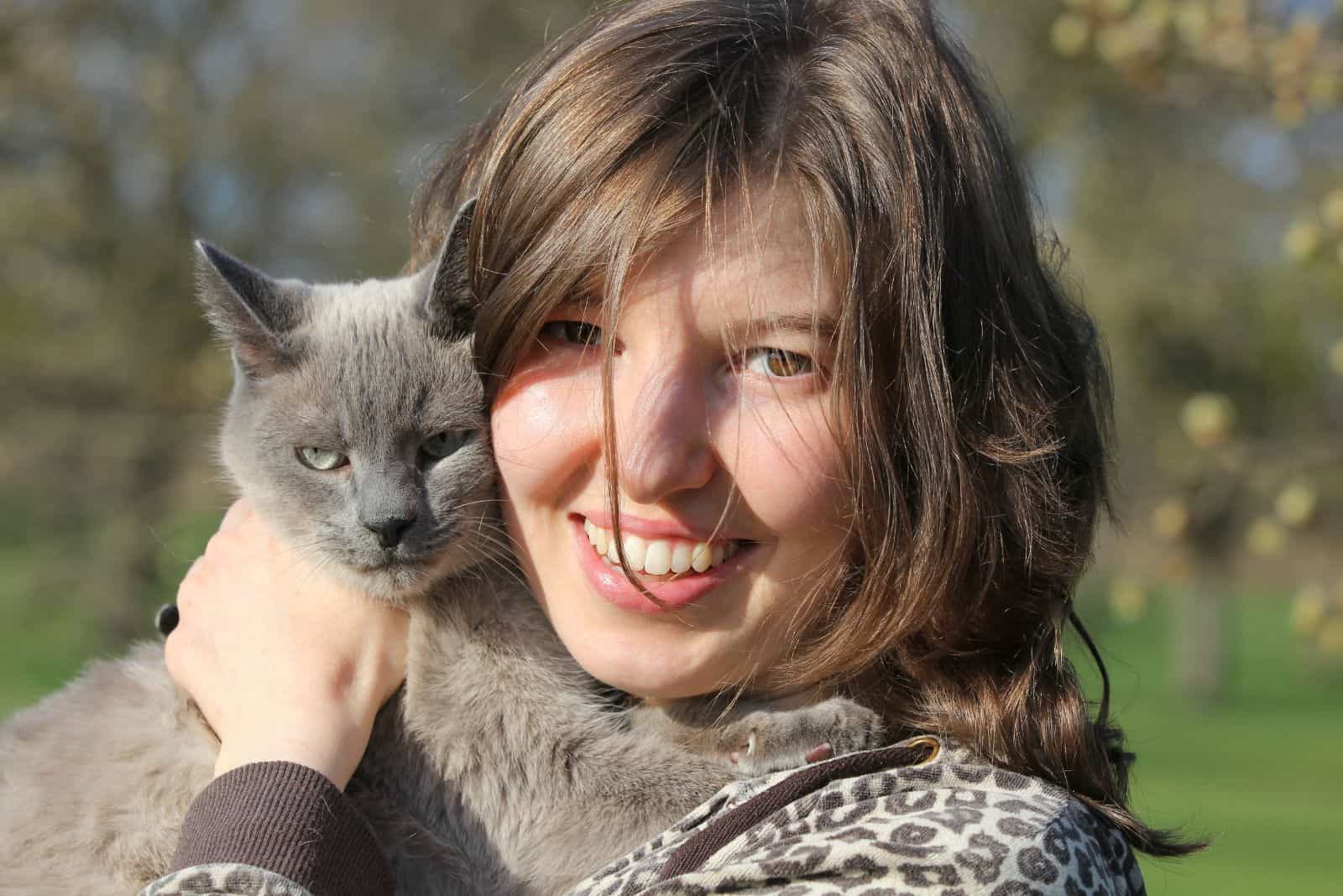 a smiling girl with black hair hugs a gray cat